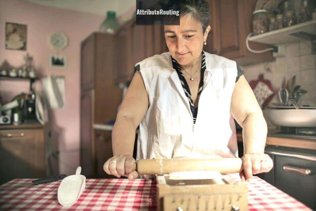 Aged female baker rolling gough with pin while cooking in cozy kitchen at home